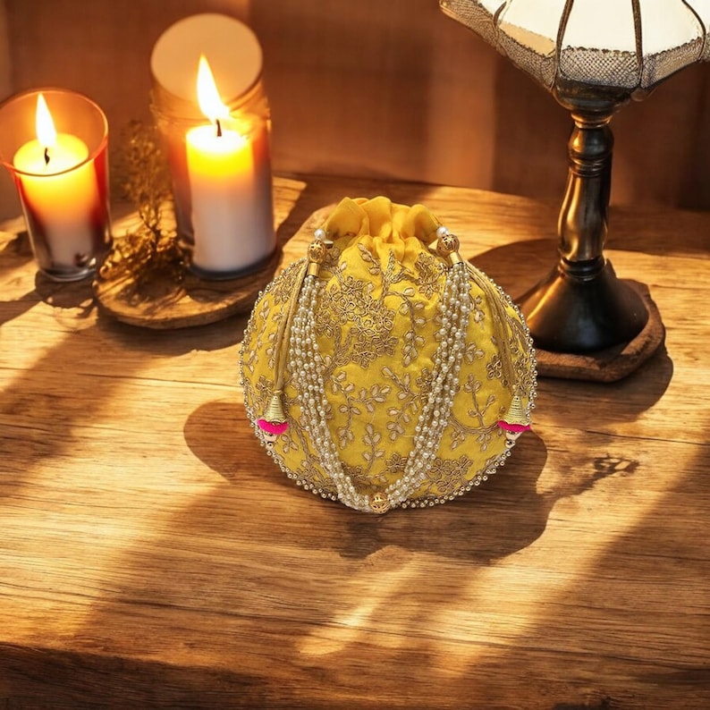 May include: A yellow drawstring bag with gold embroidery and pearl accents. The bag has a round shape and is decorated with a floral pattern.