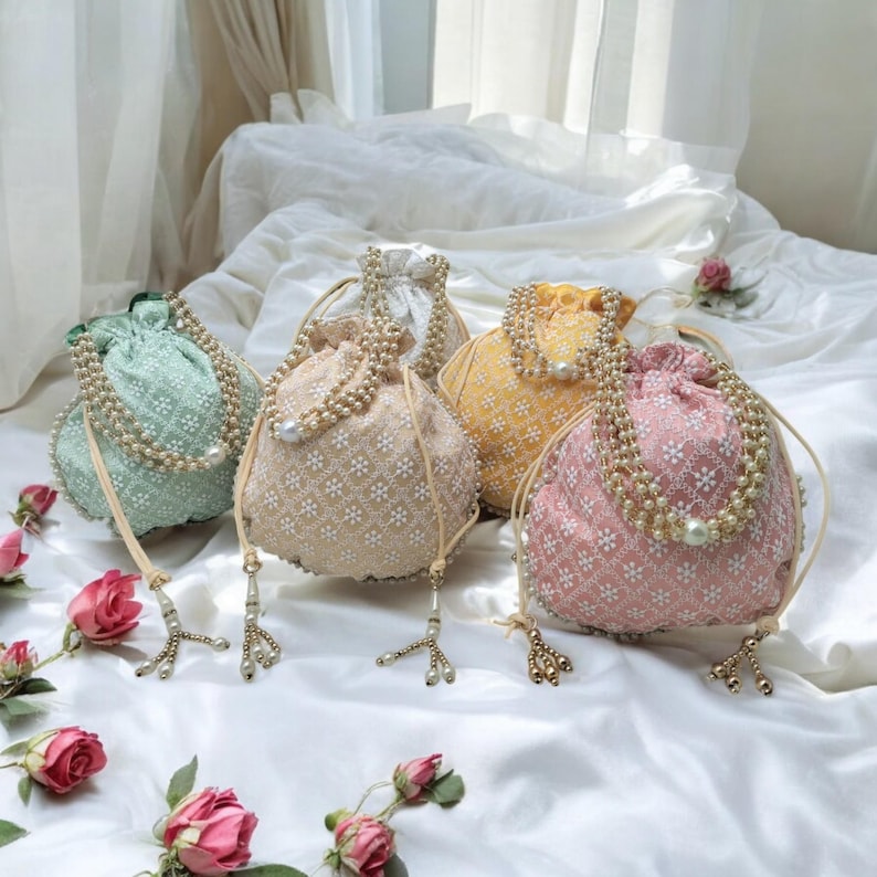 May include: Four drawstring bags with pearl embellishments. The bags are in shades of green, cream, yellow, and pink. Each bag has a tassel.