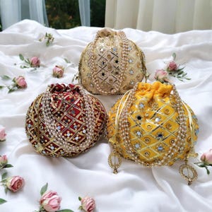 May include: Three round, beaded, drawstring bags with mirror and gold embroidery. The bags are in shades of gold, red, and cream.