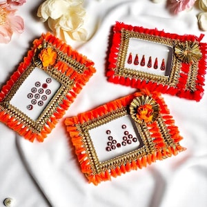 May include: Three rectangular, decorative frames with white inserts, adorned with orange fringe, gold trim, and small red embellishments. Each frame features a different arrangement of red dots. A gold and orange flower embellishes each frame.