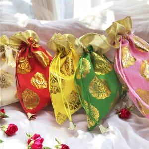 Peut inclure: Quatre petits sacs à cordon en tissu avec des accents dorés. Les sacs sont rouge, jaune, vert et rose. Les sacs sont sur une surface blanche avec quelques roses.