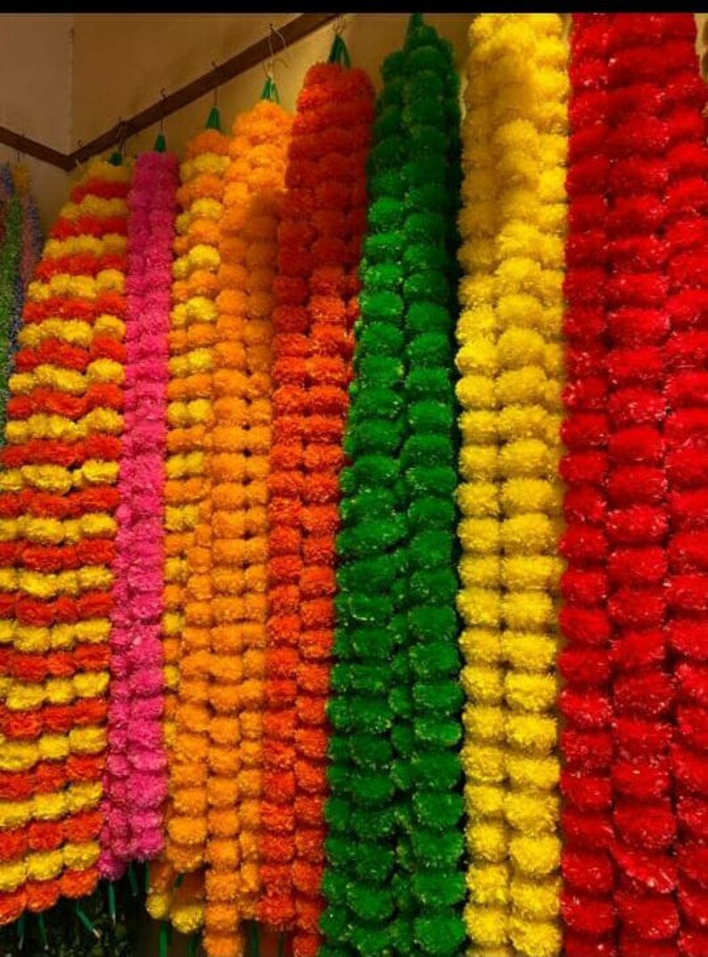 K&ouml;nnte beinhalten: Eine Sammlung bunter k&uuml;nstlicher Blumenketten, darunter Gelb, Orange, Rosa, Gr&uuml;n und Rot. Die Girlanden bestehen aus kleinen, runden Bl&uuml;tenformen und sind zu langen, dekorativen Str&auml;ngen zusammengef&uuml;gt.