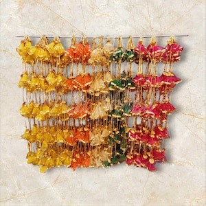 Könnte beinhalten: Eine Sammlung bunter Stoffquasten, die an einer Schnur hängen. Die Quasten sind in den Farben Gelb, Orange, Grün und Pink.