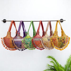 Puede incluir: Siete bolsos de mano de tela de patchwork coloridos con flecos colgando de una barra de metal. Los bolsos están hechos de diferentes telas y colores, incluyendo rojo, naranja, amarillo, verde, azul y morado.