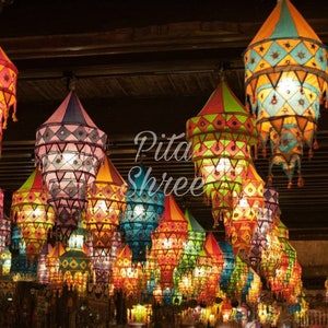 Può includere: Un soffitto pieno di lanterne colorate in tessuto con motivi. Le lanterne sono appese al soffitto e sono illuminate, creando un'atmosfera calda e accogliente. Il testo "Pita Shree" è visibile sullo sfondo.