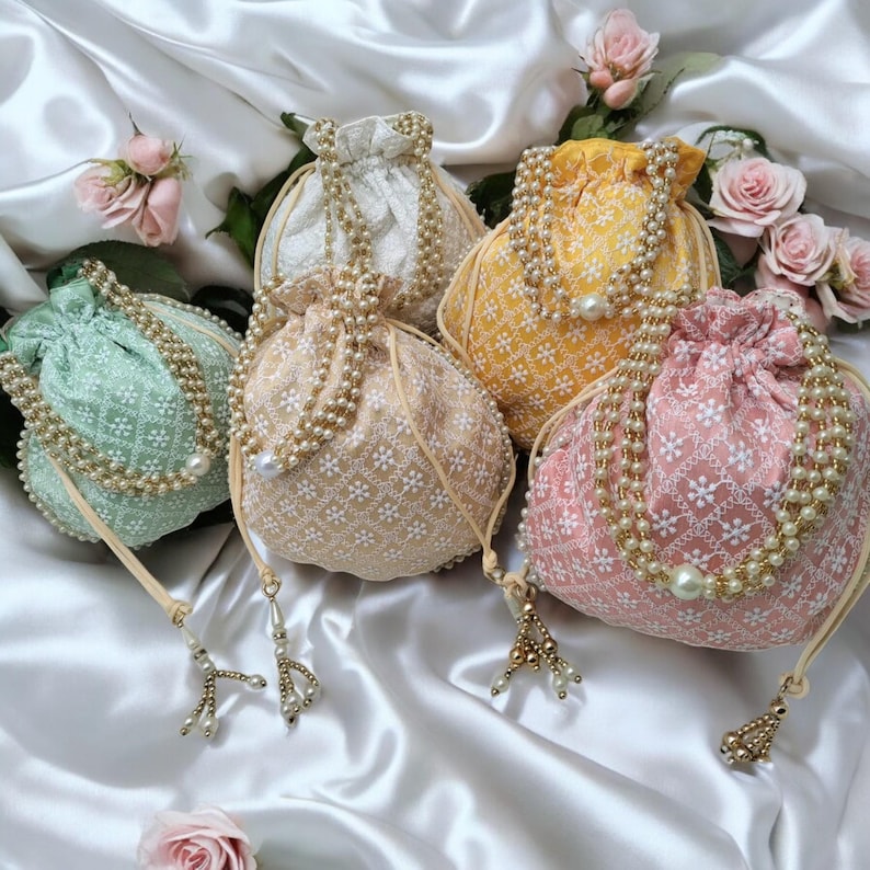 May include: Five drawstring bags with pearl embellishments. The bags are in various colors, including green, yellow, pink, and white. Each bag has a floral pattern and a pearl tassel.