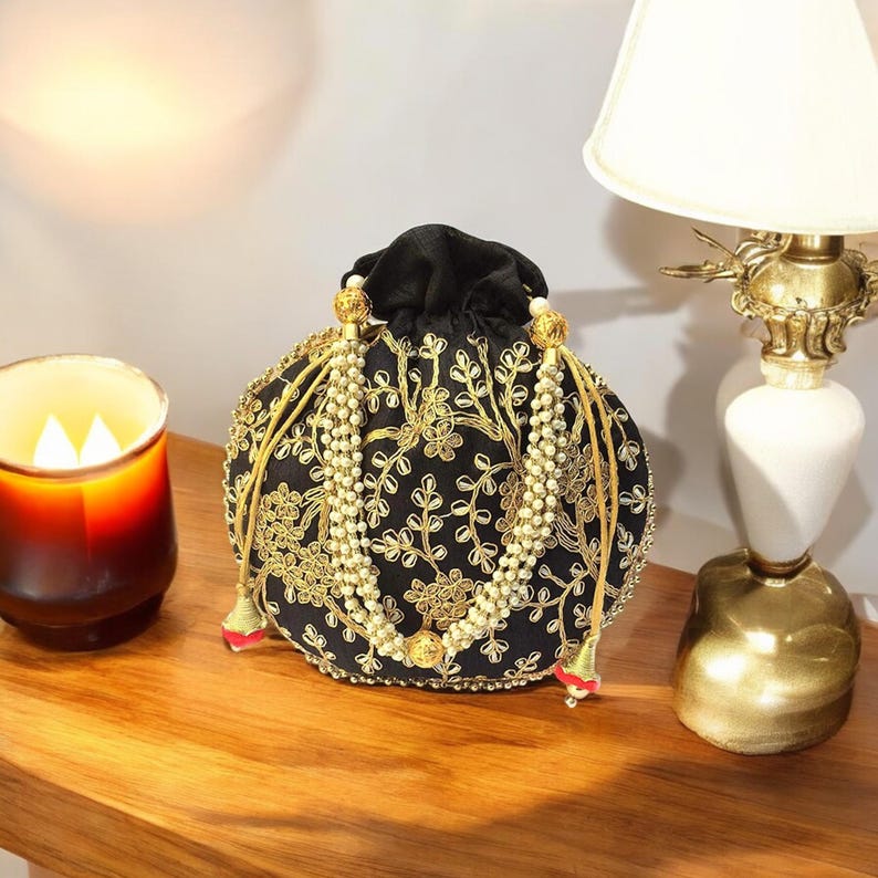 May include: A black drawstring bag with gold embroidery and pearl accents. The bag has a round shape and is decorated with a floral pattern.