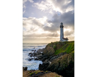 May include: A white lighthouse with a black roof stands tall on a rocky cliff overlooking a choppy ocean. The sky is a mix of blue and gray with white clouds.