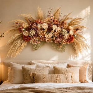 May include: A large wall-mounted floral arrangement featuring a mix of dried pampas grass, beige palm spears, and artificial roses in shades of cream, dusty rose, and burnt orange, creating a wide, arched display of textured botanical elements.