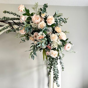 May include: A wedding arch decorated with a cascading arrangement of blush pink and white roses, greenery, and eucalyptus.