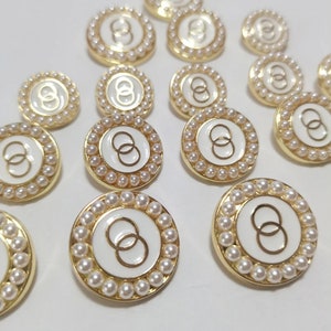 May include: A collection of white and gold round buttons with a pearl border. Each button features a double ring design in the center.