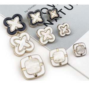 May include: Assortment of white and black decorative buttons with a floral design. The buttons have a gold trim and a pearl-like finish.