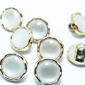 May include: A set of six oval-shaped buttons with a white, pearlescent center and a gold-colored metal rim. The buttons have a slightly raised, rounded center.