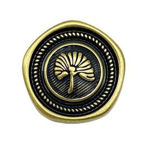 Puede incluir: Un botón de metal dorado con un centro negro que presenta un diseño de árbol estilizado. El botón tiene un borde de cuerda.