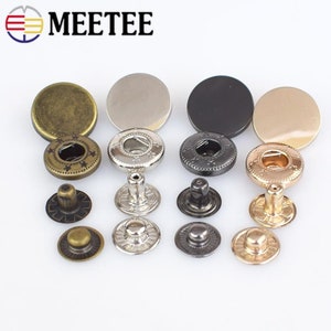 May include: Assortment of metal snap buttons in gold, silver, and black finishes. Each button has a decorative design and includes a top and bottom piece.