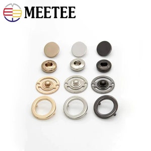 Può includere: Assortimento di bottoni a pressione in metallo in finiture oro, argento e nero. I bottoni sono di diverse dimensioni e stili, tra cui rotondi, piatti e decorativi.