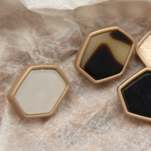 Puede incluir: Cuatro botones hexagonales con ribete dorado. Los botones están hechos de diferentes materiales, incluyendo blanco, negro y caparazón de tortuga marrón.
