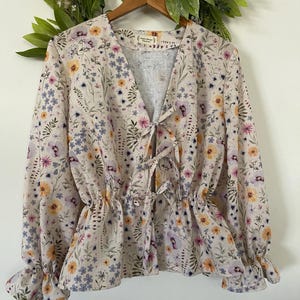 May include: A beige floral print blouse with a V-neckline and long sleeves. The blouse has a tie at the front and a ruffled hem.