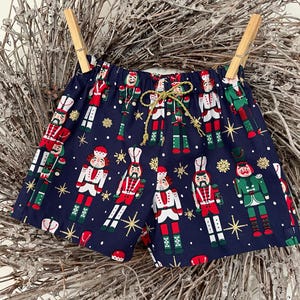 May include: Navy blue shorts featuring a festive pattern of nutcracker soldiers and gold stars.
