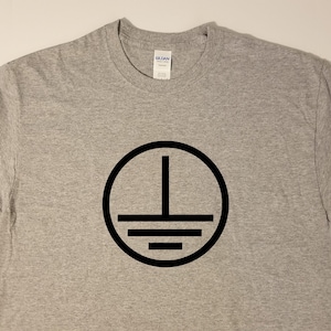 May include: A gray t-shirt with a black circle containing a vertical line and three horizontal lines. The symbol is a ground symbol.