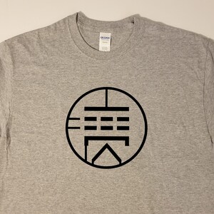 May include: A gray t-shirt with a black circle design featuring a stylized symbol with lines and squares.