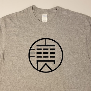 May include: A gray t-shirt with a black circle design featuring a stylized symbol with lines and squares.