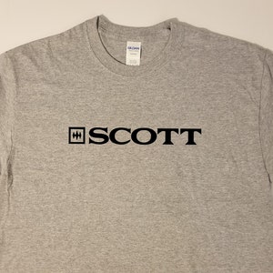 Puede incluir: Una camiseta gris con un logotipo negro que dice "SCOTT" con un cuadrado que contiene una "H" estilizada a la izquierda de la palabra.