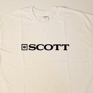 Puede incluir: Camiseta blanca con un logotipo negro que dice "SCOTT" con un peque&ntilde;o cuadrado negro que contiene tres l&iacute;neas horizontales a la izquierda de la palabra.