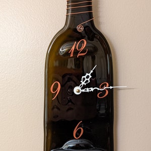 May include: A dark green glass wine bottle clock with copper wire accents and white clock hands. The numbers 12, 9, 3, and 6 are printed in orange on the bottle.