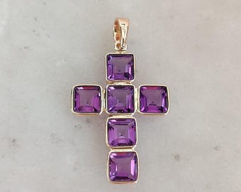 Könnte beinhalten: Ein goldener Kreuzanhänger mit sechs quadratischen Amethyst-Edelsteinen. Der Anhänger befindet sich auf einem weißen Hintergrund.
