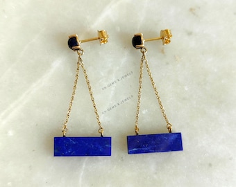 Può includere: Un paio di orecchini d'oro con un pendente a barra in lapislazzuli blu e una perla nera nella parte superiore di ogni orecchino.