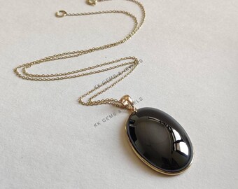 May include: A gold chain necklace with an oval black gemstone pendant. The pendant is set in a gold bezel.