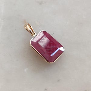May include: A gold pendant featuring a large, rectangular, red ruby gemstone.