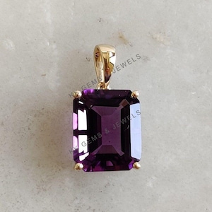 May include: A gold pendant featuring a large, deep purple, emerald-cut gemstone. The pendant is set in a simple gold frame.