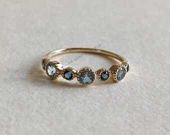 Può includere: Un anello a fascia d'oro con sette pietre preziose blu incastonate in una montatura a bezel. L'anello è un gioiello delicato e femminile.