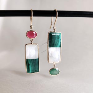 May include: A pair of gold earrings with green and white rectangular stones and a red oval stone. The earrings have a drop design with a smaller green stone hanging from the bottom of the rectangular stone.