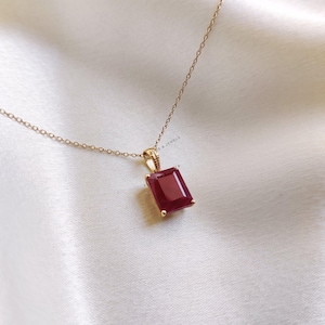 May include: A gold chain necklace with a red gemstone pendant. The gemstone is a rectangular emerald cut.