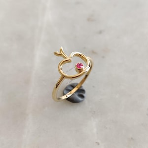 May include: A gold ring with a red gemstone in the center, shaped like an apple with a stem and leaf.
