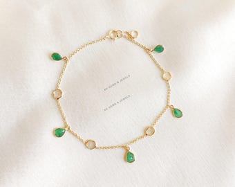 Könnte beinhalten: Ein goldenes Kettenarmband mit grünen und weißen Edelstein-Akzenten. Das Armband hat eine zarte Kette mit kleinen, tropfenförmigen grünen Edelsteinen und runden weißen Edelsteinen.