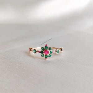 May include: A gold ring featuring a red ruby and green emeralds set in a starburst design.
