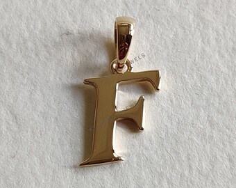 May include: Gold-toned pendant charm in the shape of the letter F. The pendant has a simple, elegant design.
