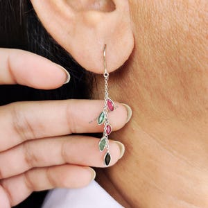May include: Silver dangle earrings with a chain and multiple teardrop-shaped gemstones in shades of green, red, and black.