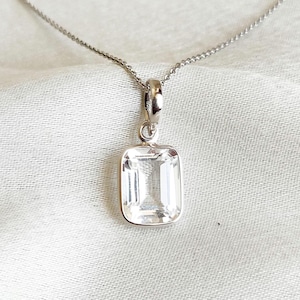 May include: A silver chain necklace with a clear rectangular pendant. The pendant is a large, faceted gemstone.
