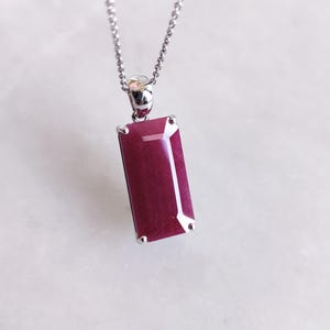 May include: A silver chain necklace with a deep red rectangular pendant. The pendant has a faceted cut and is set in a silver bezel.