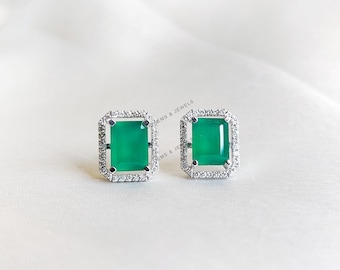 Könnte beinhalten: Ein Paar silberne Ohrringe mit einem grünen Edelstein, der in einem quadratischen Rahmen mit einem Heiligenschein aus kleinen Diamanten gefasst ist.