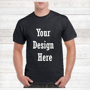 May include: Black t-shirt with the text "Your Design Here" in white block letters. The shirt is a crew neck style and appears to be made of a soft material. The background is a white wood panel.