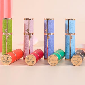 May include: A selection of colourful, textured perfume atomisers in shades of green, pink, blue, and white. The atomisers have gold detailing and a cylindrical shape. Some atomisers have initials or names engraved on the base.