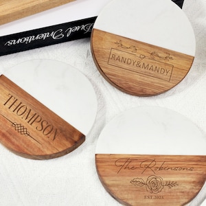 May include: Three round coasters with a two-tone design. The bottom half is wood-toned, and the top half is white. Each coaster has personalized text: "THOMPSON", "RANDY&MANDY", and "The Robinsons EST.2025".