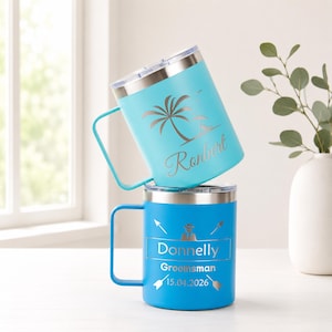 May include: Two insulated travel mugs. One is light blue with a palm tree and the name "Ronbert". The other is blue with the name "Donnelly", the word "Groomsman", and the date "15.04.2026". Both mugs have silver rims and handles.