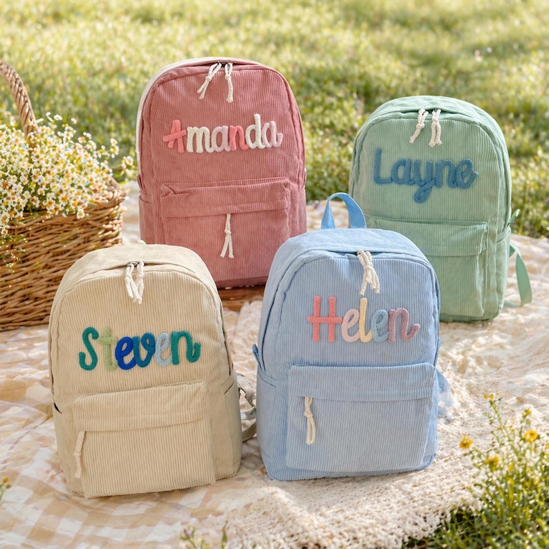 Puede incluir: Cuatro mochilas de pana en colores pastel: rosa, verde, azul y beige. Cada mochila tiene un nombre bordado: "Amanda", "Layne", "Helen" y "Steven". Las mochilas tienen un bolsillo frontal y una cremallera superior.
